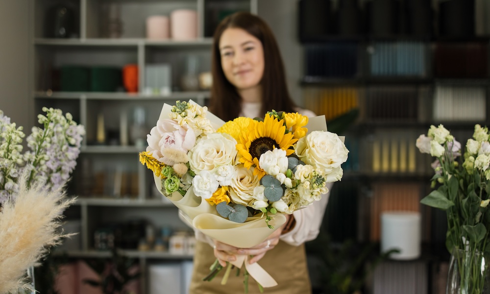 Focus on bouquet. Portrait of female florist in apron working in flower shop.